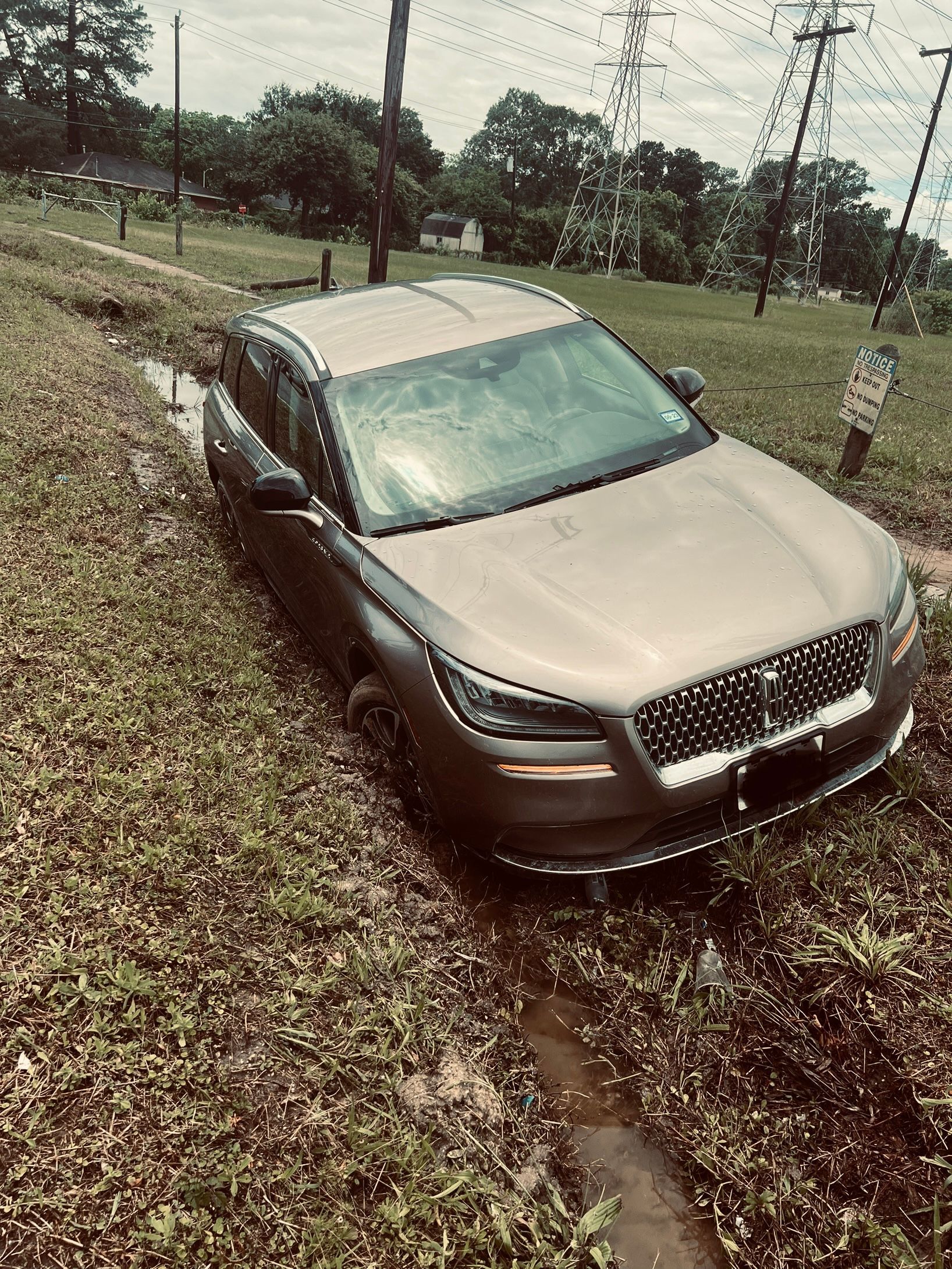 Silver sedan stuck in a muddy grassy ditch on a rural roadside after rain