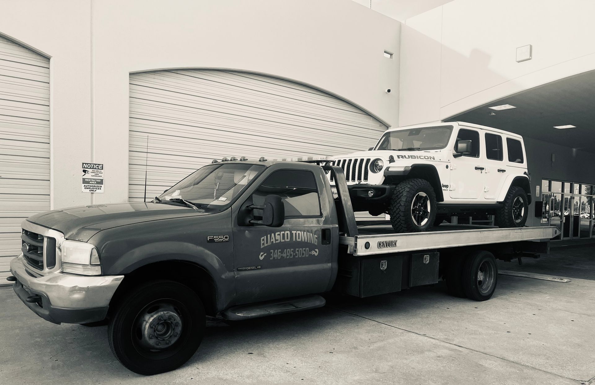 Gray flatbed tow truck carrying a white Jeep inside a garage-like bay