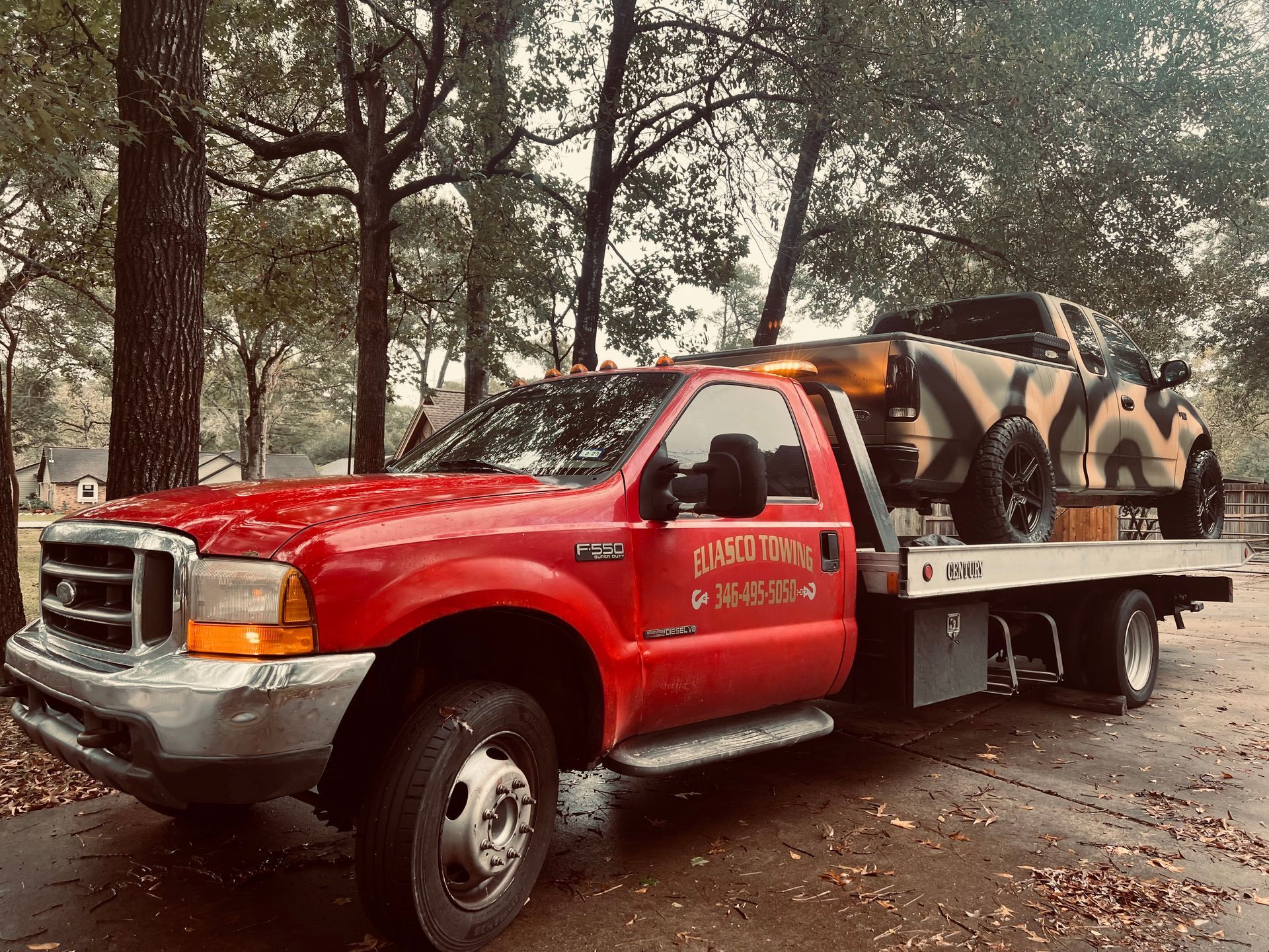 Red tow truck carrying an overturned car on a forest road in autumn.