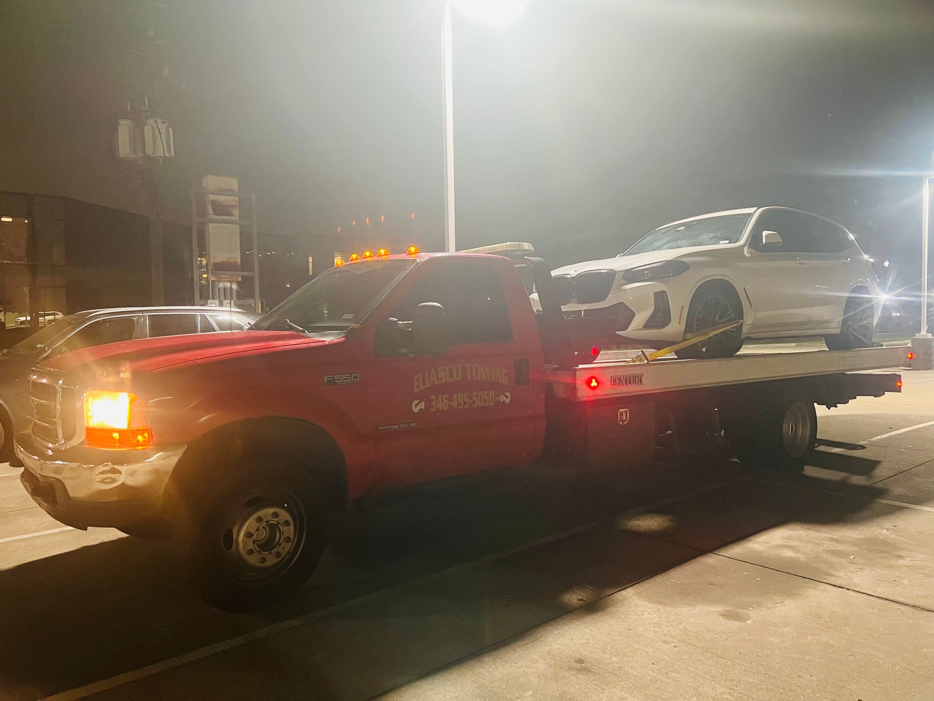 Tow truck carrying a white SUV at night with bright headlights and streetlights