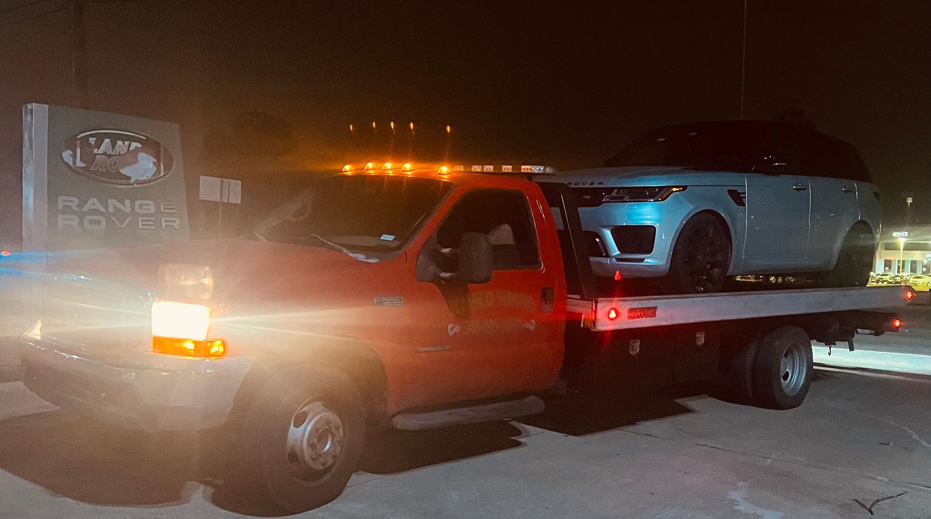 Tow truck hauling a black pickup at night, with bright amber lights and snow on the ground