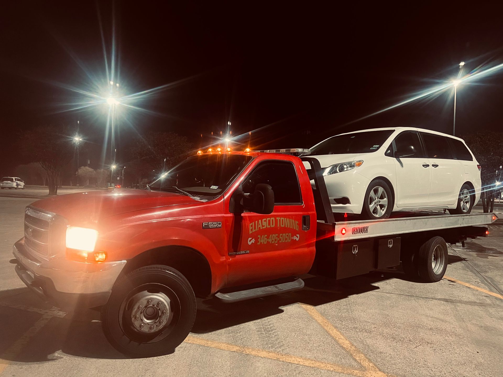 Red tow truck carrying a white minivan at night in a parking lot