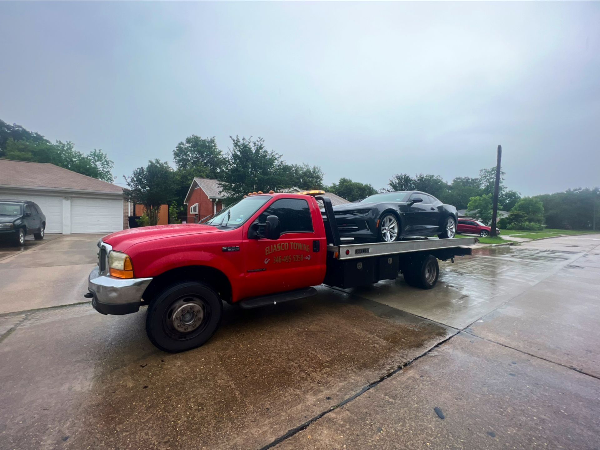 Red tow truck carrying a car on a wet street in a rainy neighborhood