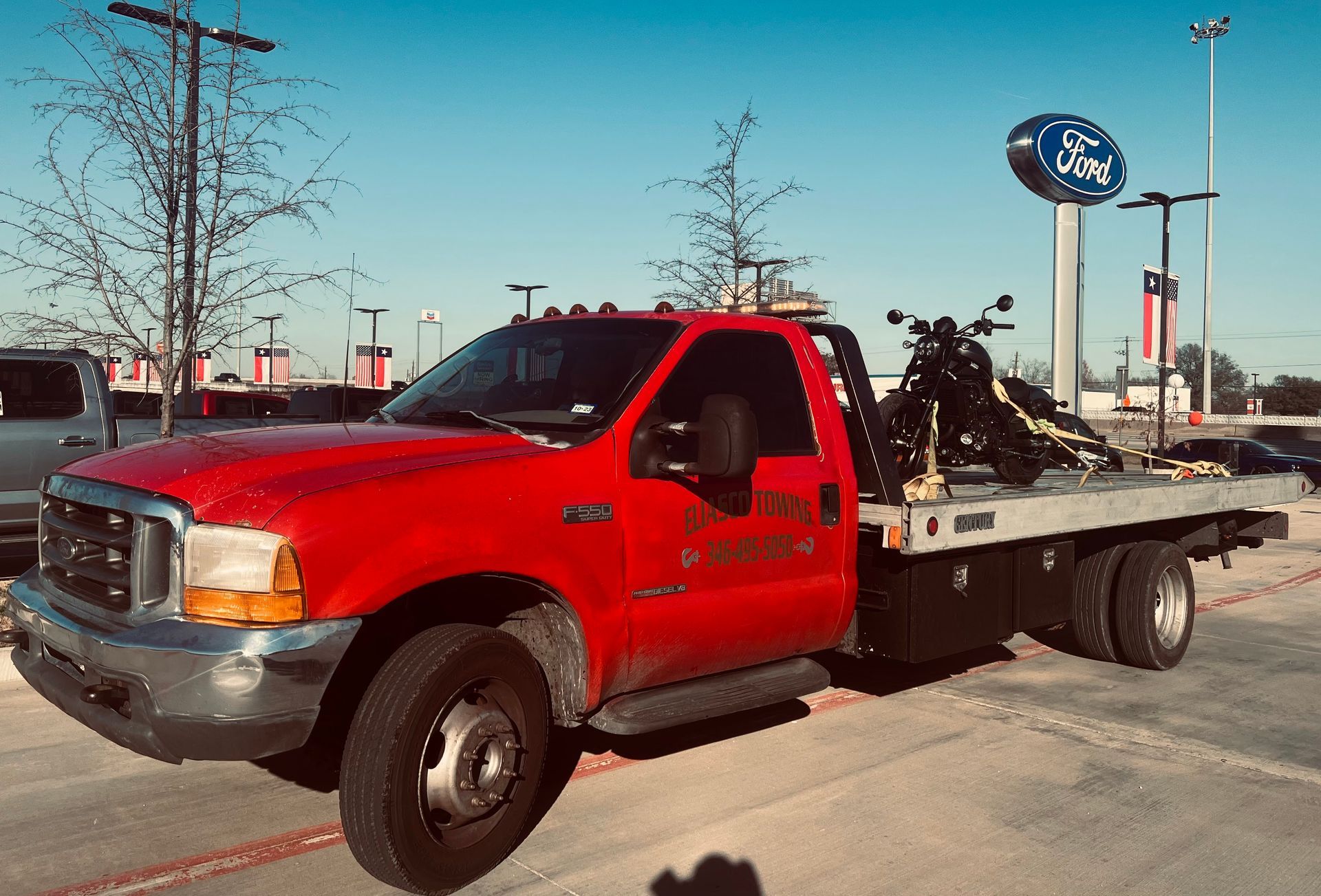 Red flatbed tow truck carrying a Christmas tree in a parking lot under a blue sky.