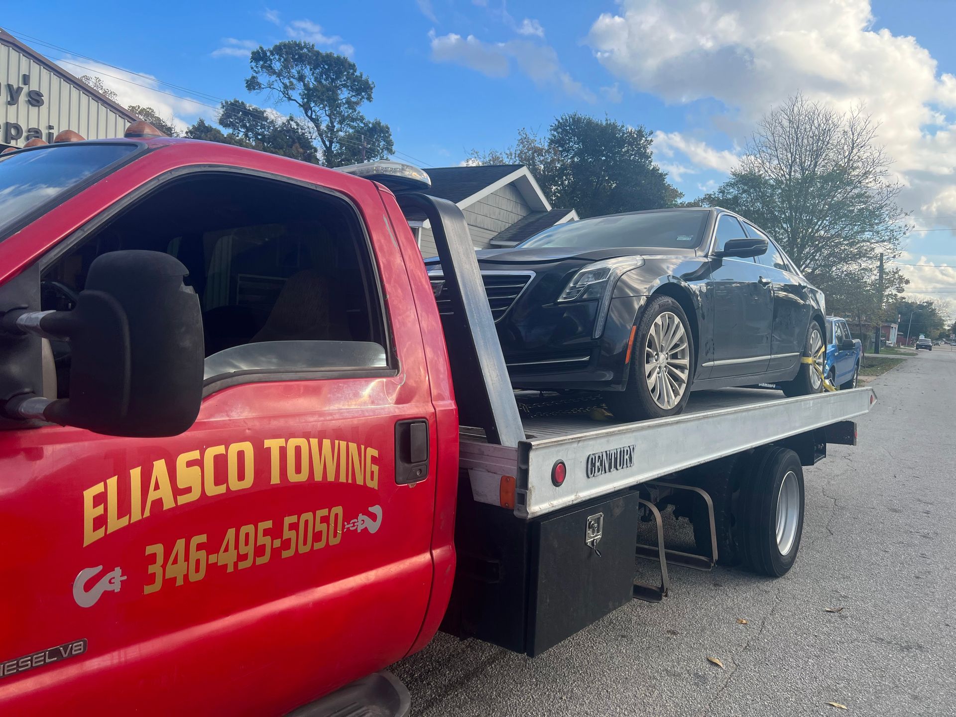 Red tow truck carrying a black sports car on a flatbed under a sunny sky