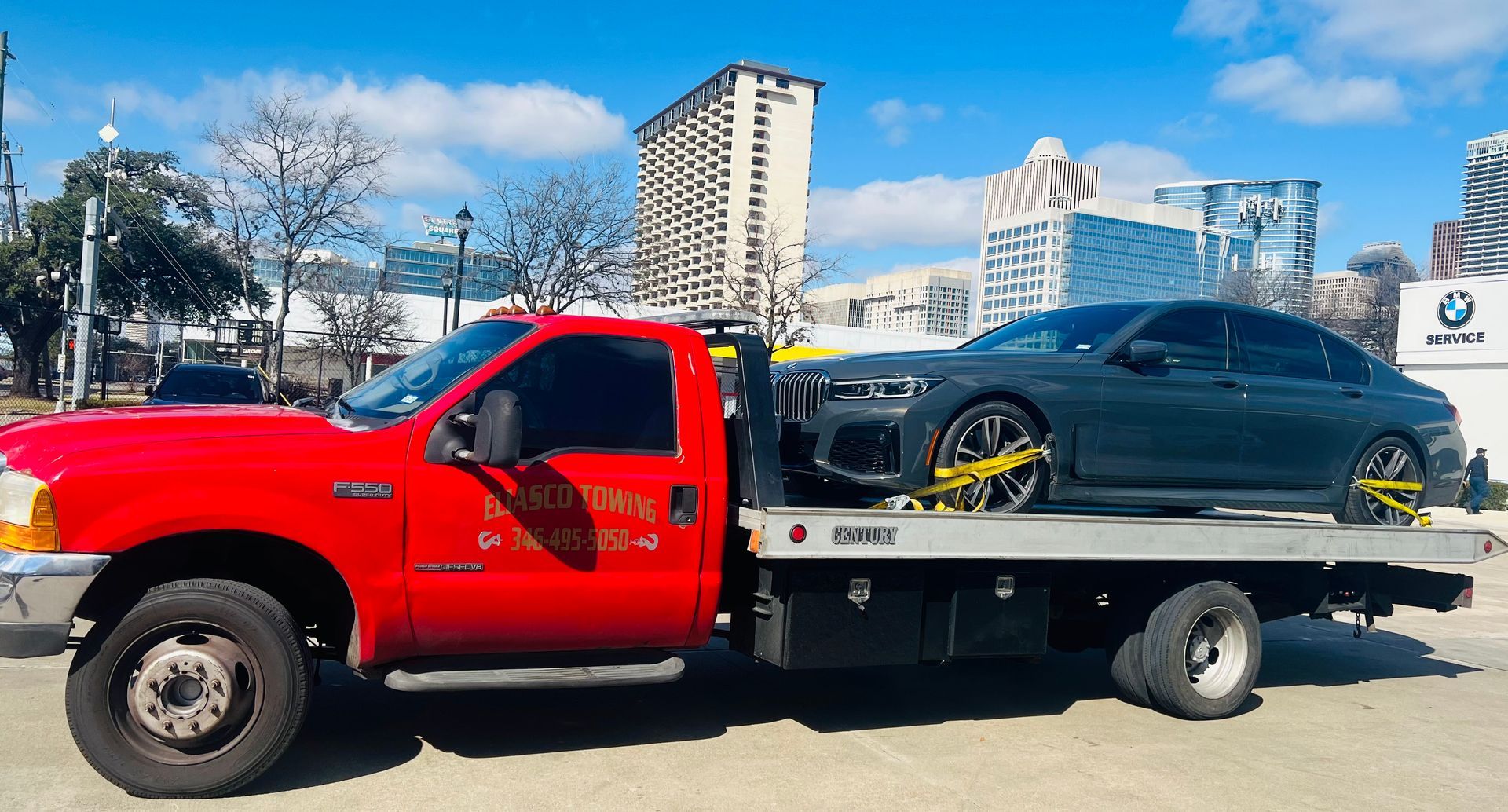 Red tow truck carrying a black sports car on a flatbed in an urban street.