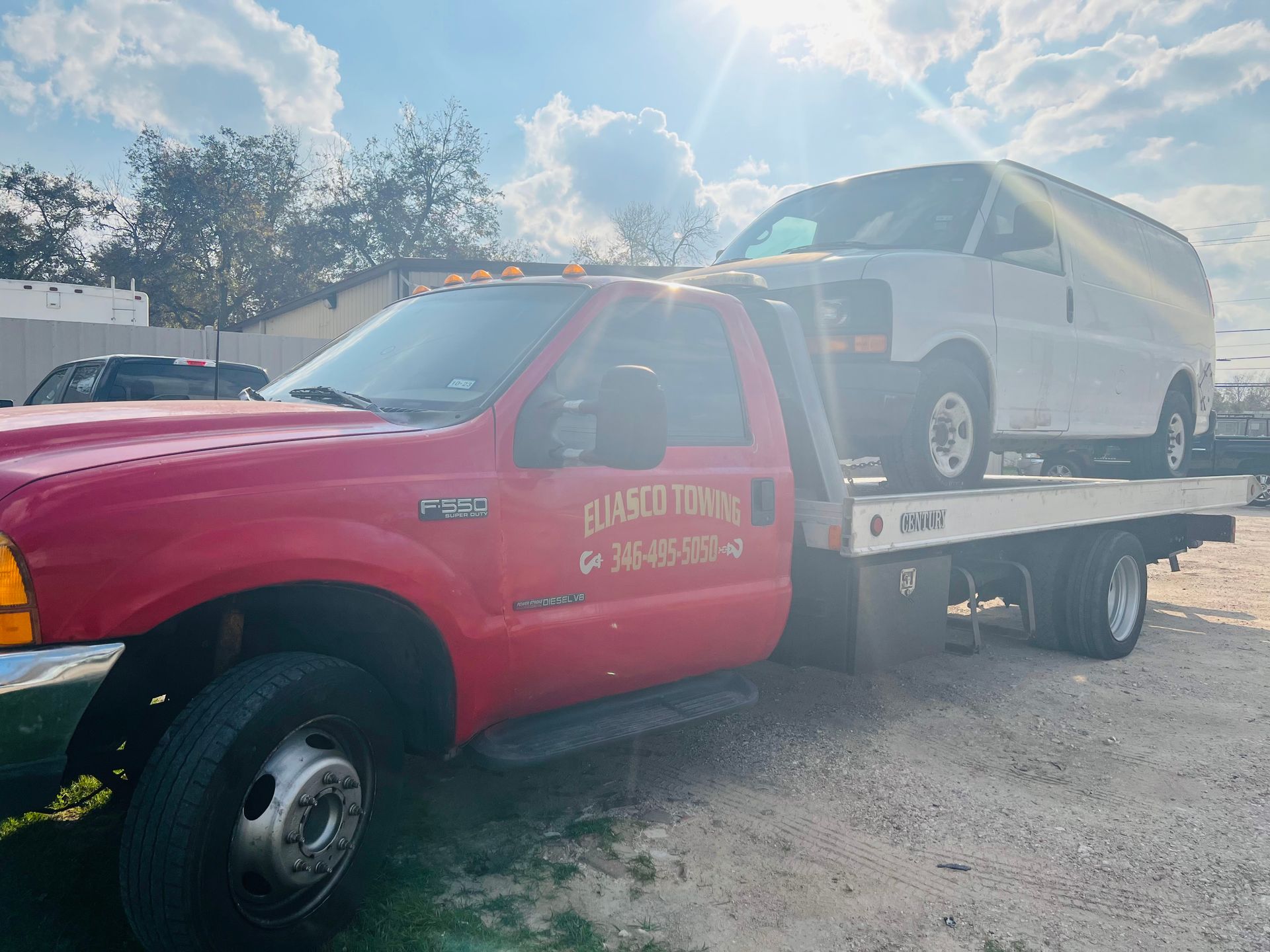Tow truck carrying a white SUV on a flatbed in a sunny parking lot