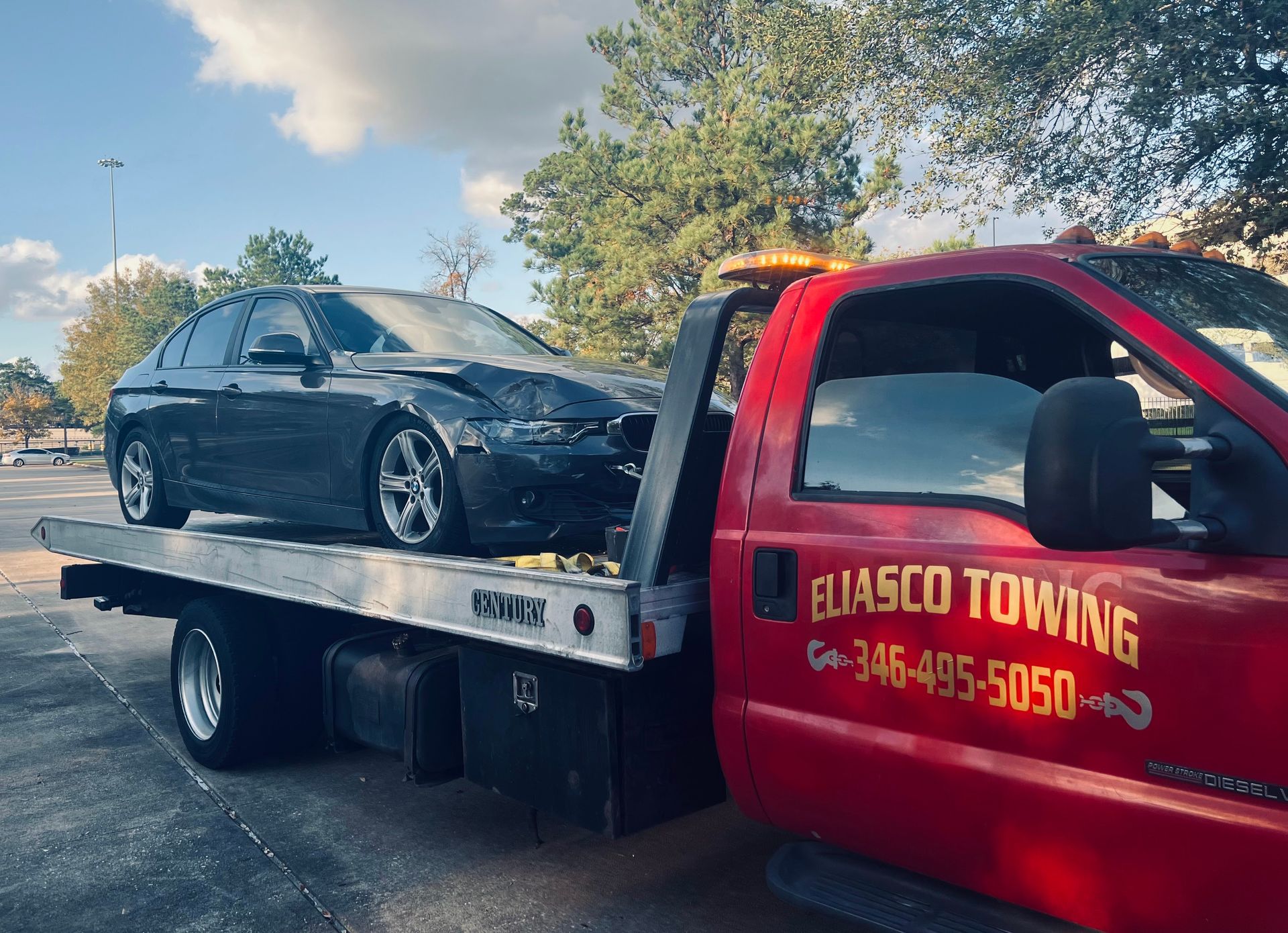 Tow truck hauling a black sedan, with red tow truck cab and blue sky in the background