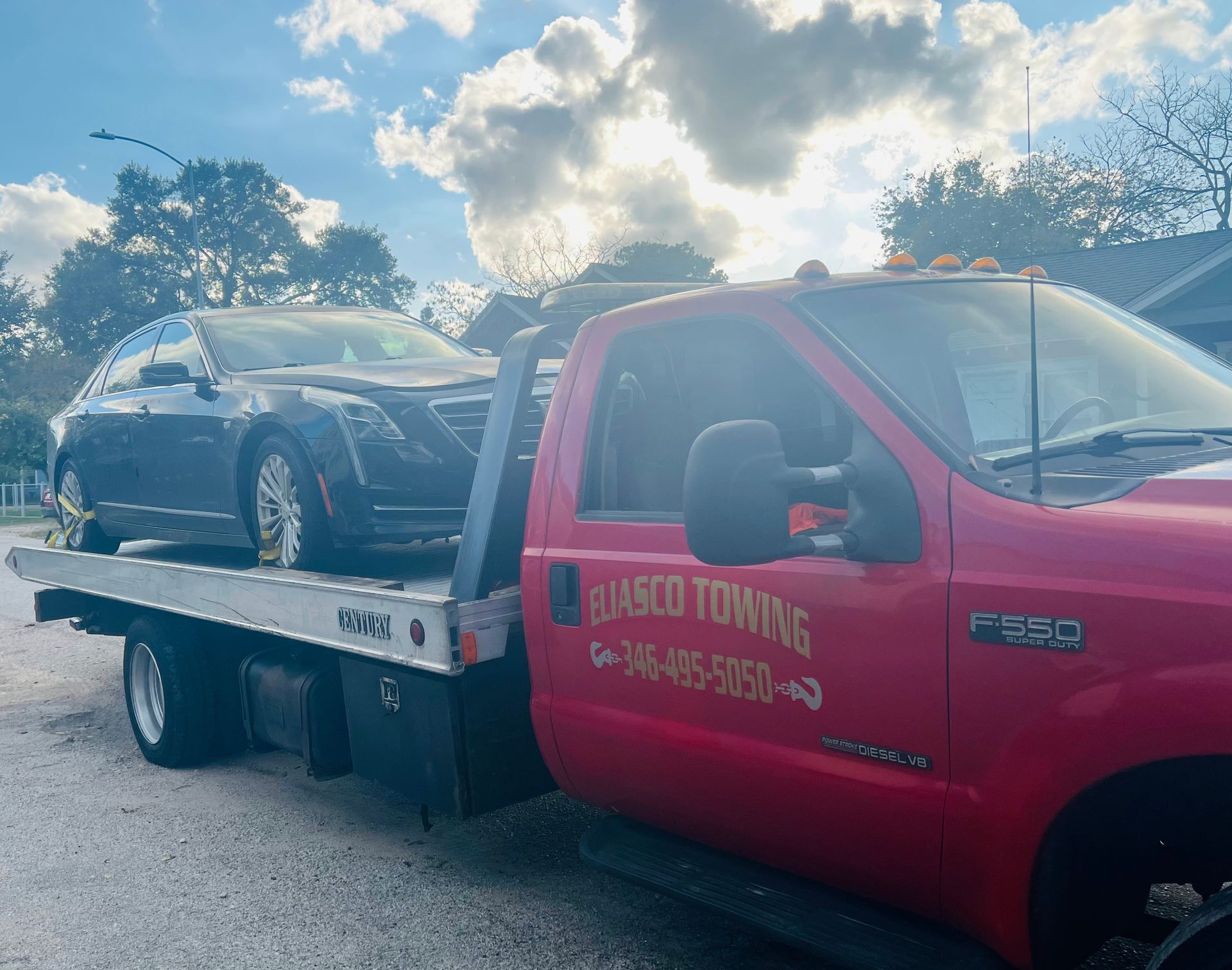 Red towing truck hauling a black sedan on a flatbed under a cloudy sky.