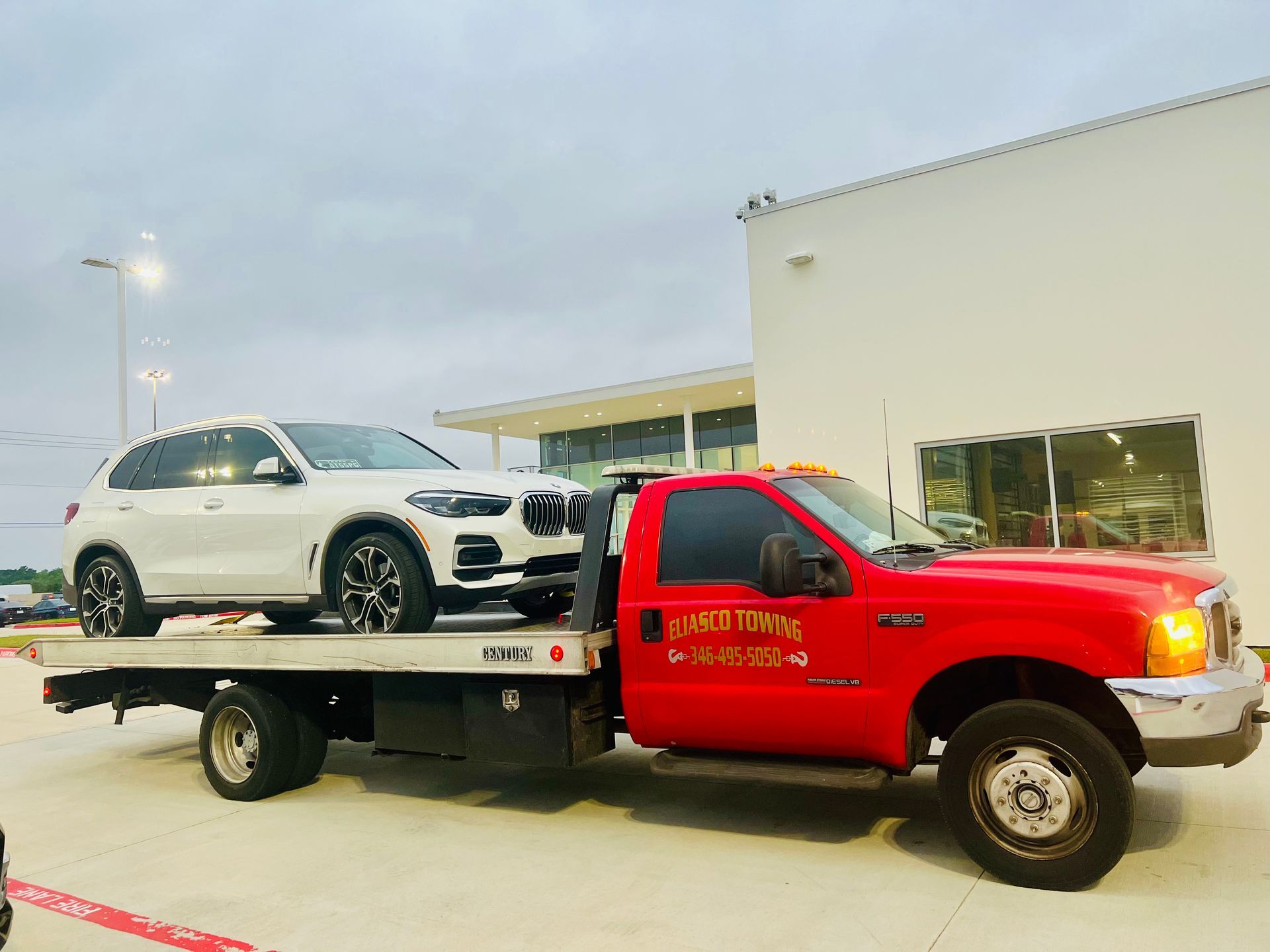 Red tow truck carrying a white SUV outside a building at dusk