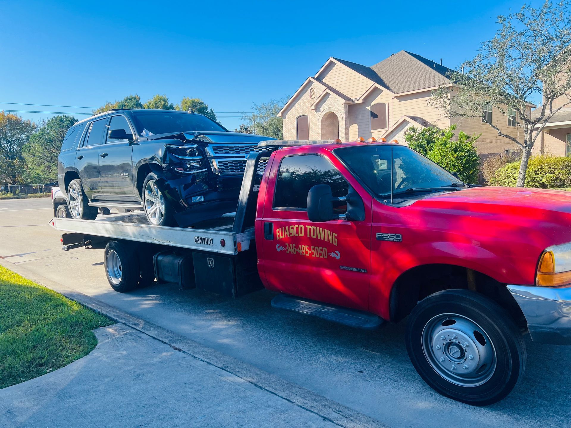 Red tow truck hauling a black SUV on a sunny suburban driveway