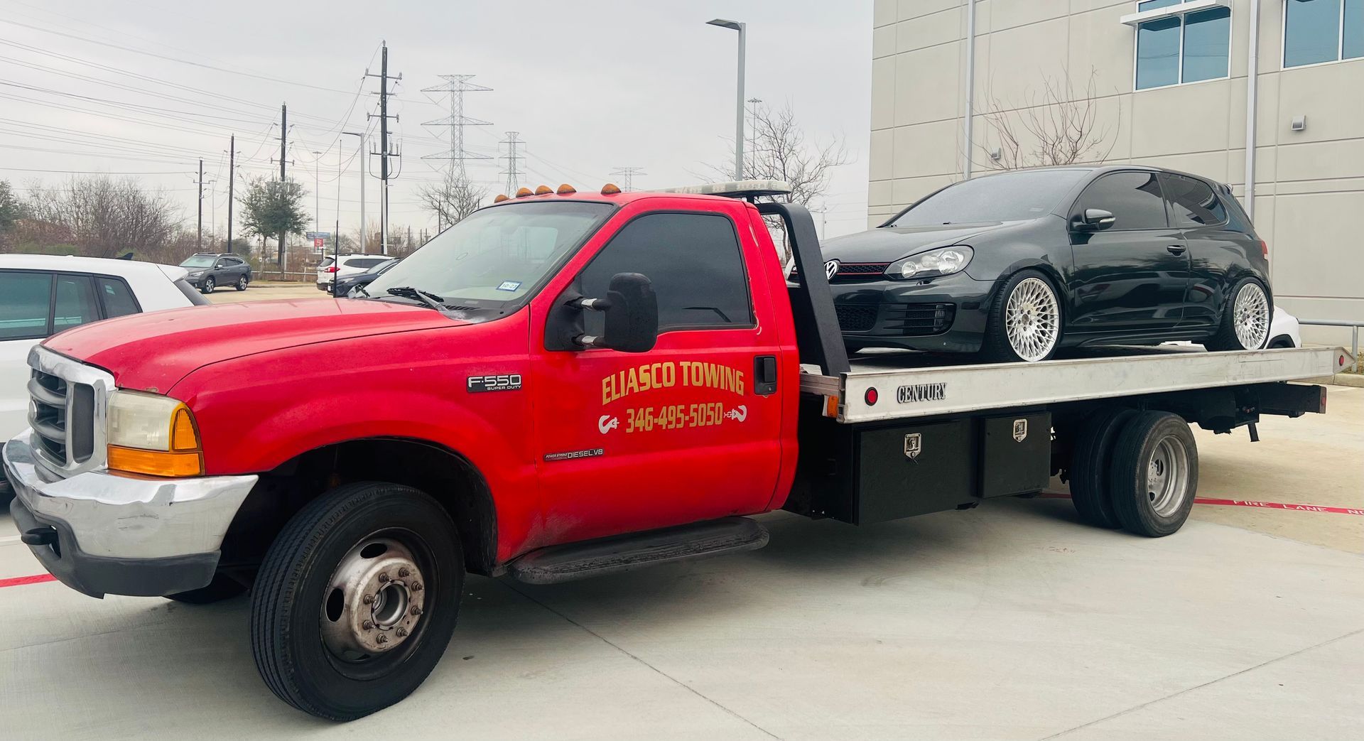 Red tow truck hauling a black car on a flatbed in a parking lot