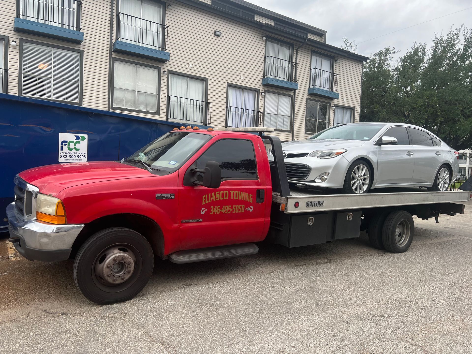 Red tow truck carrying a silver sedan on a flatbed in front of row houses
