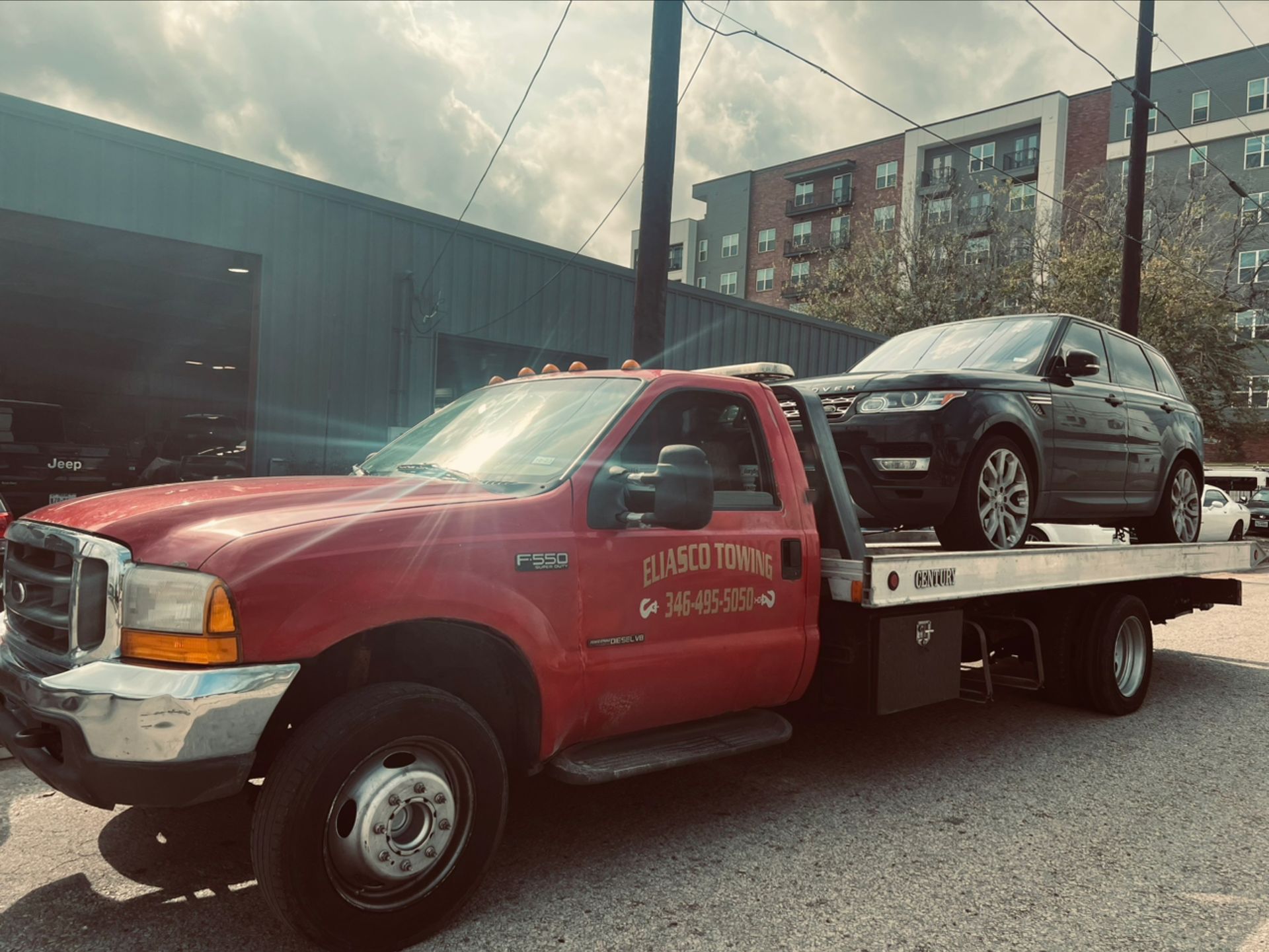 Red tow truck hauling a black SUV on a flatbed in a parking lot