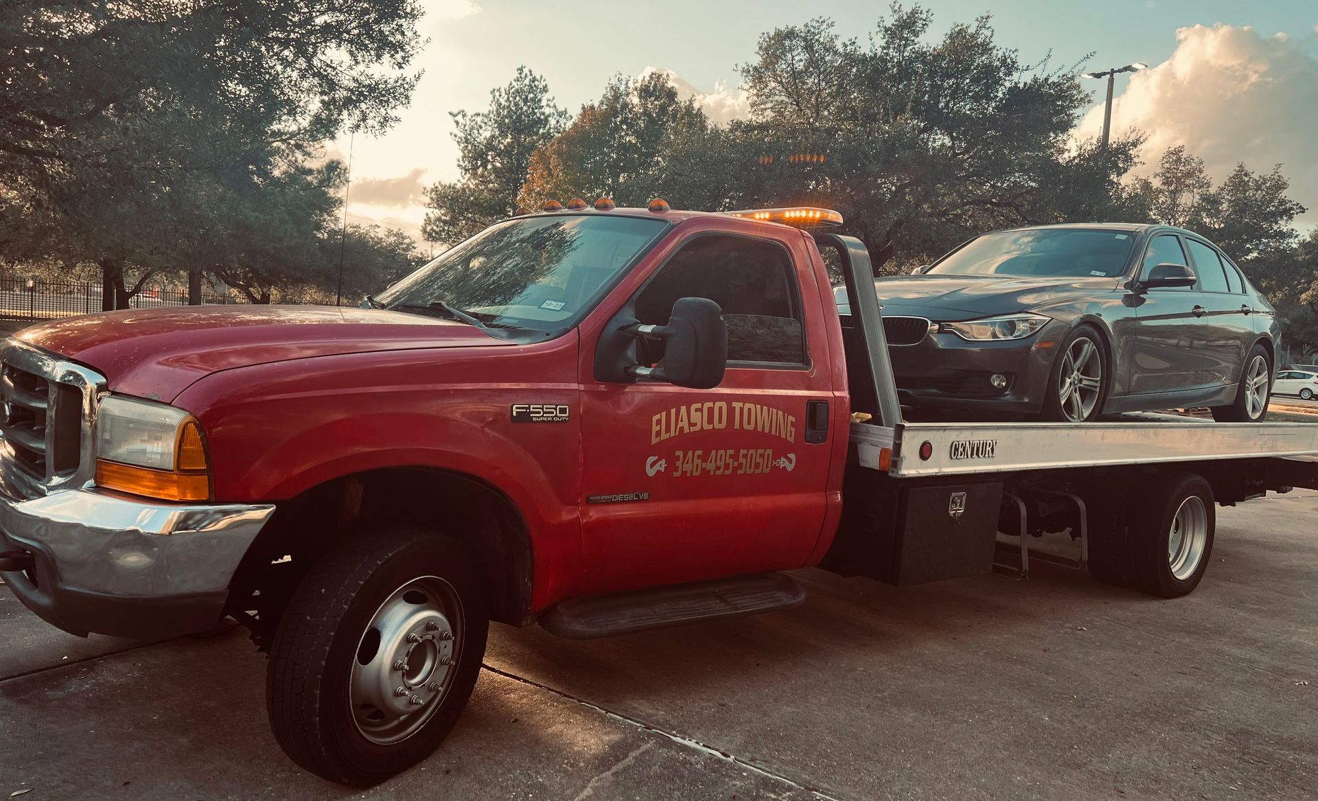 Red tow truck hauling a black car on a flatbed at sunset