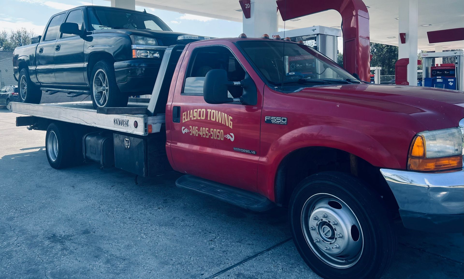 Red tow truck carrying a black SUV at a gas station pump