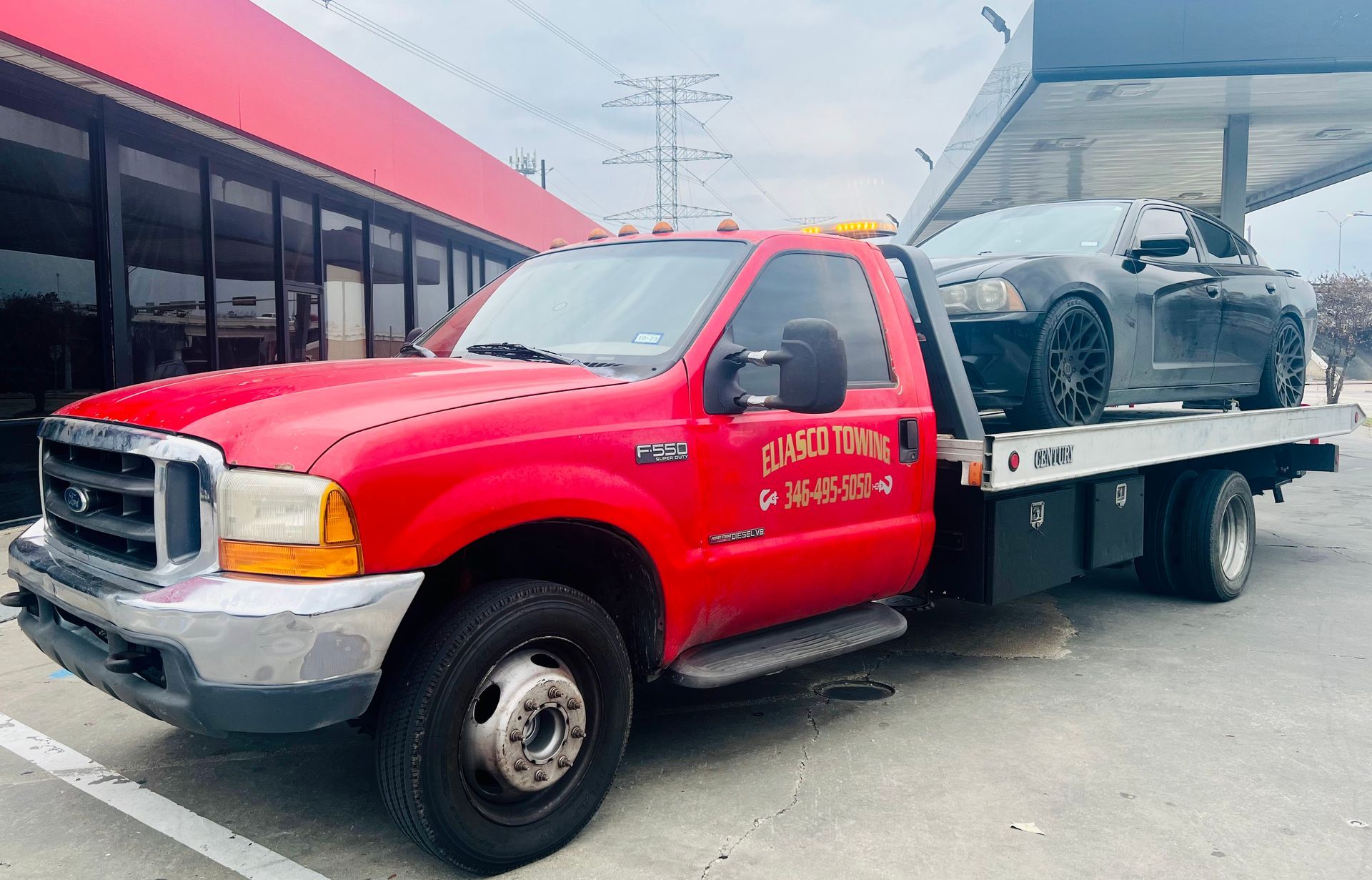 Red tow truck hauling a gray car on a flatbed in a parking lot
