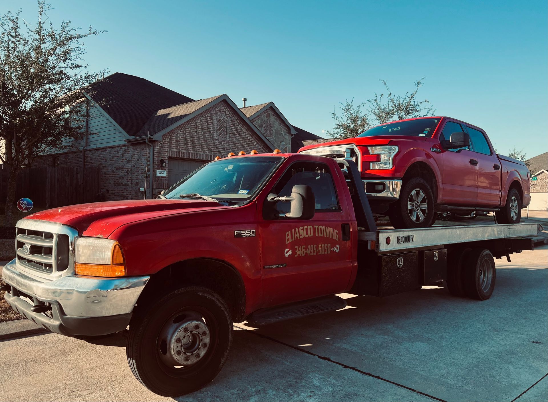 Red tow truck carrying a red SUV on a flatbed in a residential driveway.