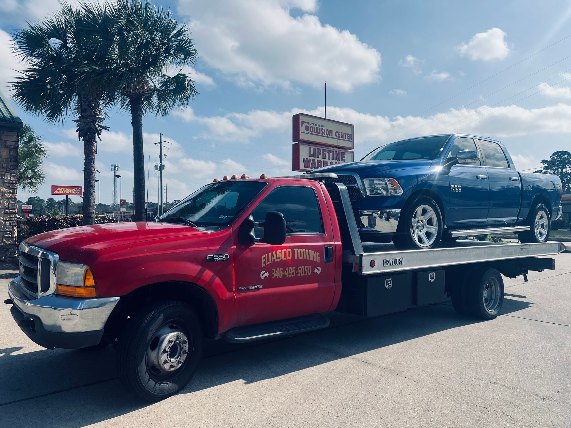 Red tow truck hauling a blue sedan on a sunny street
