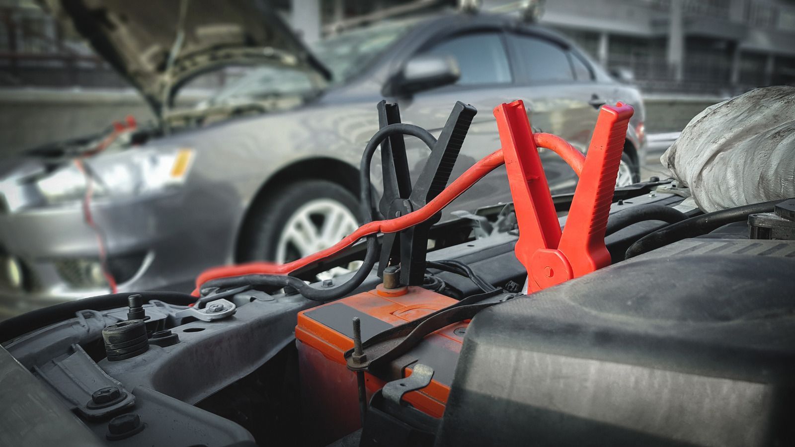 Car battery jump-start cables clipped to a car engine in a roadside breakdown scene