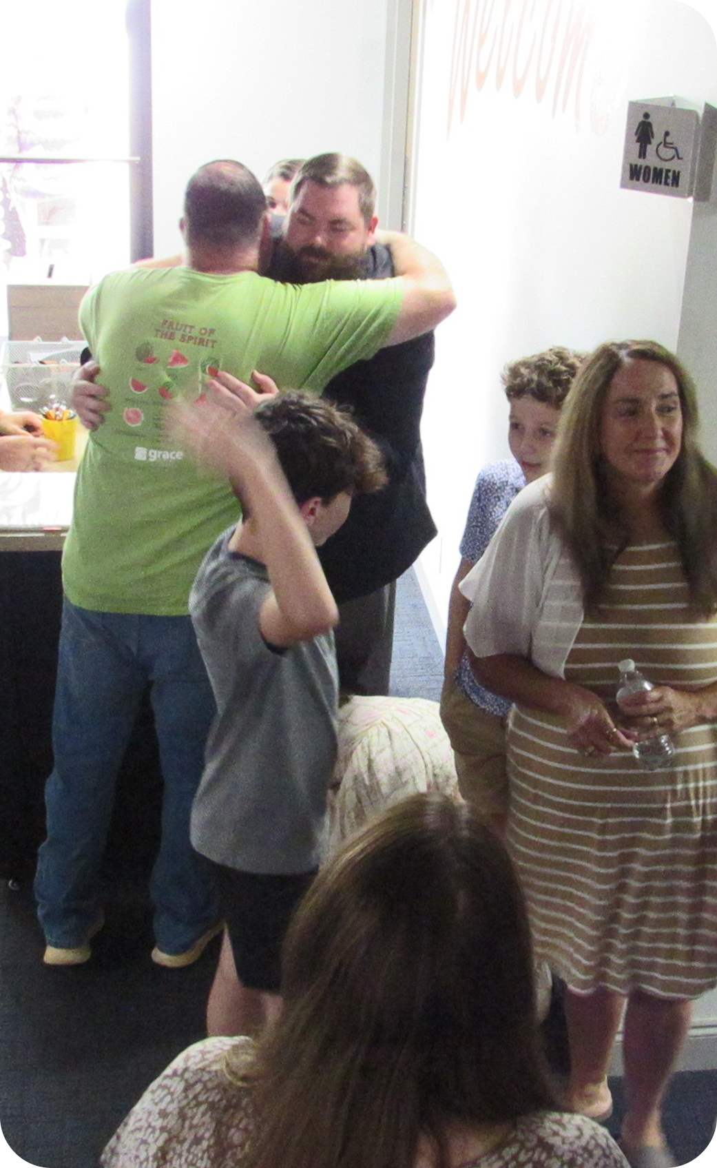 People greeting and chatting at an indoor gathering, with drinks and a casual buffet in the background.