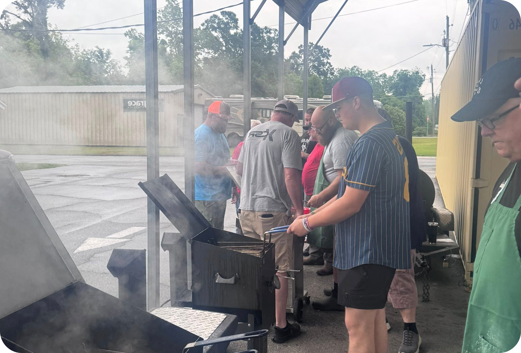 People cooking at outdoor barbecue grills in a smoky covered area