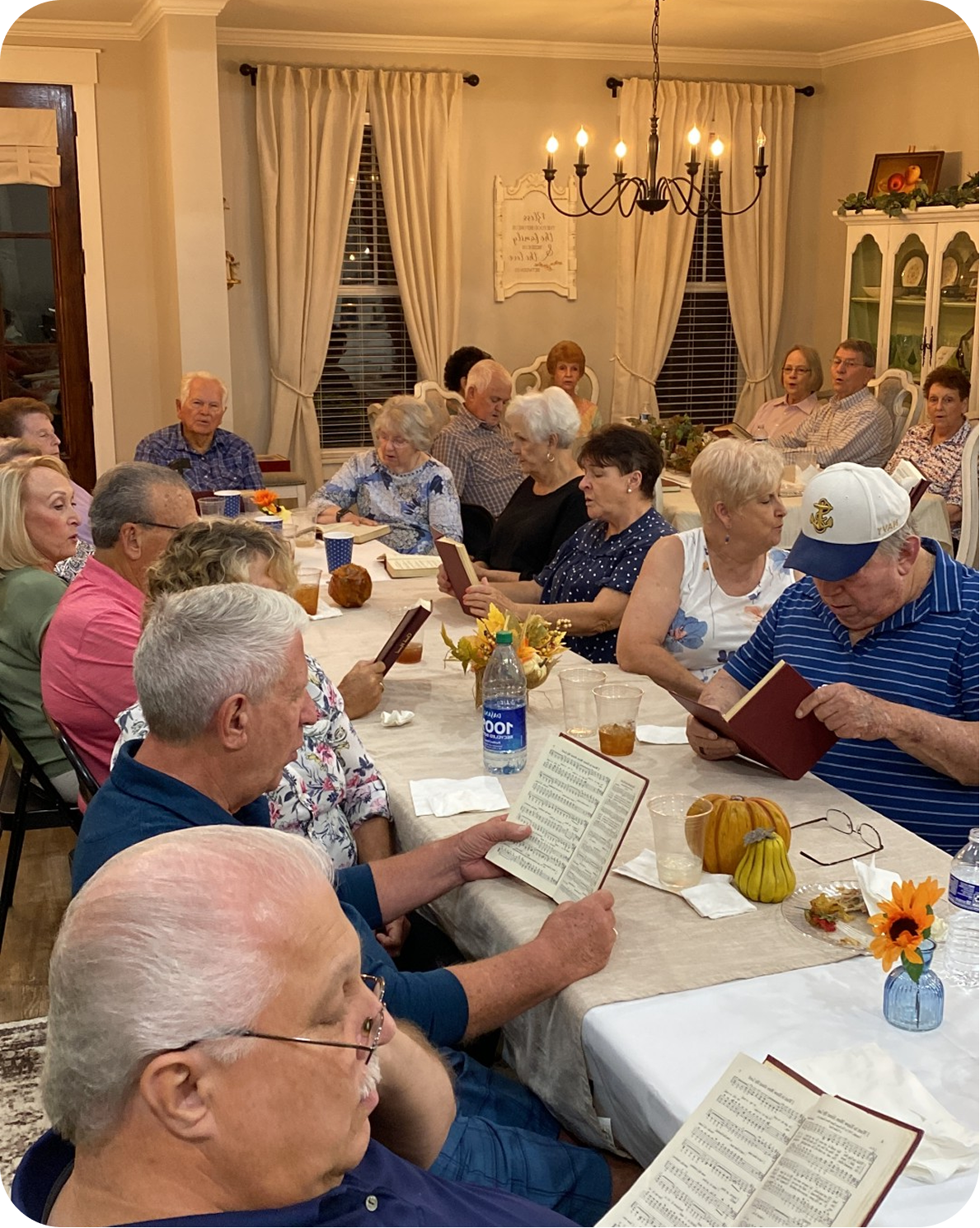 Group of people gathered around a long table reading sheets in a warmly lit dining room