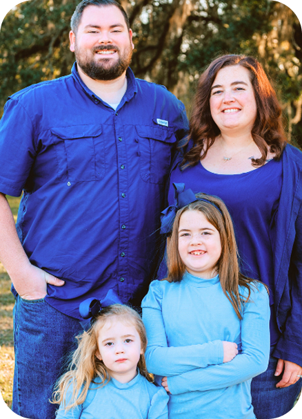 Family of four posing outdoors, with two adults in blue and two children in front.