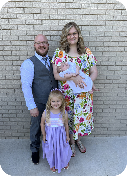 Family of four posing in front of a brick wall, with two children in pastel outfits.