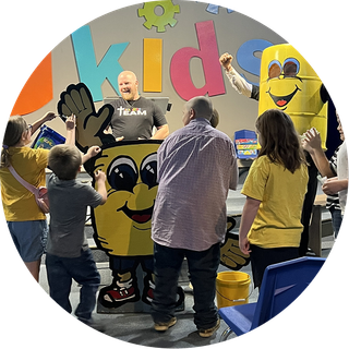 People waving at smiling staff behind a kids event booth with colorful cartoon decorations