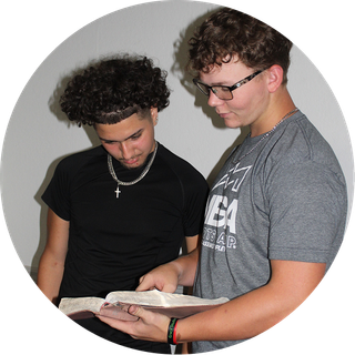 Two people reading a book together indoors, one pointing at the open pages.