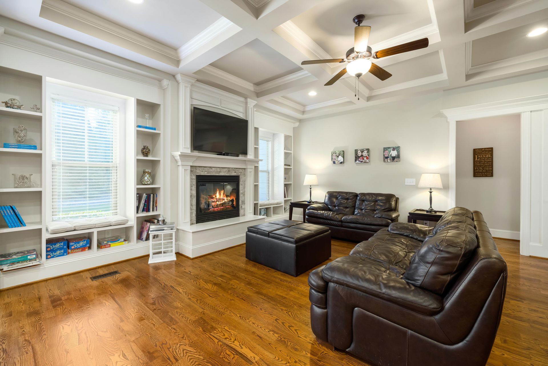 A living room with hardwood floors , a couch , chairs , a fireplace and a ceiling fan.