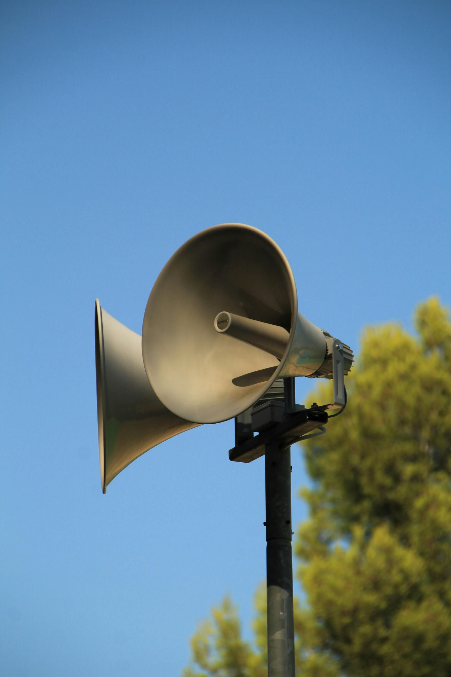 A pair of speakers on a pole with trees in the background.