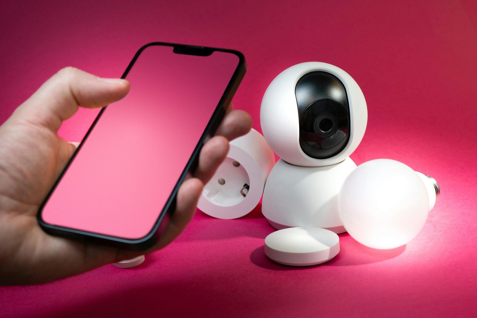 A person is holding a smart phone next to a camera and a light bulb.
