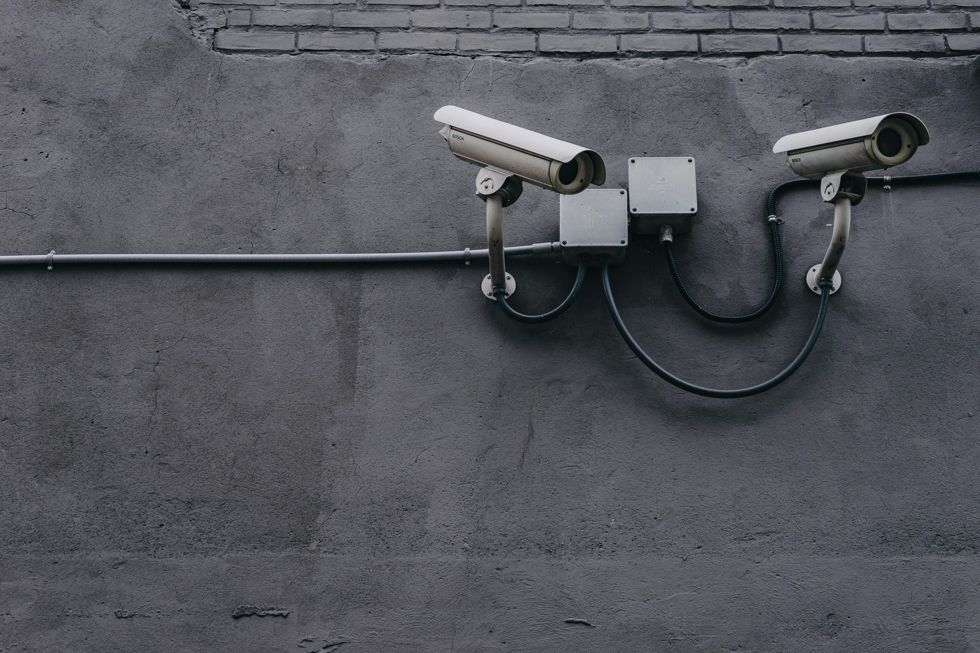 Two security cameras are attached to a brick wall.