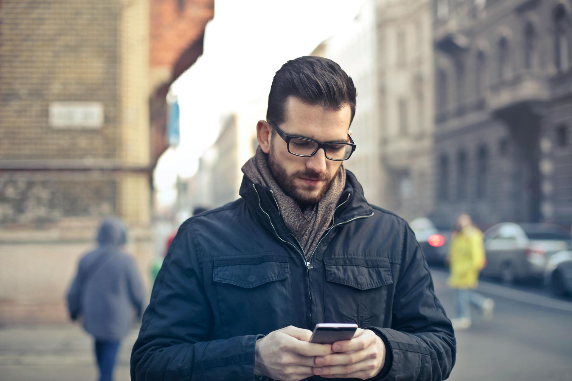 A man is standing on a city street looking at his cell phone.