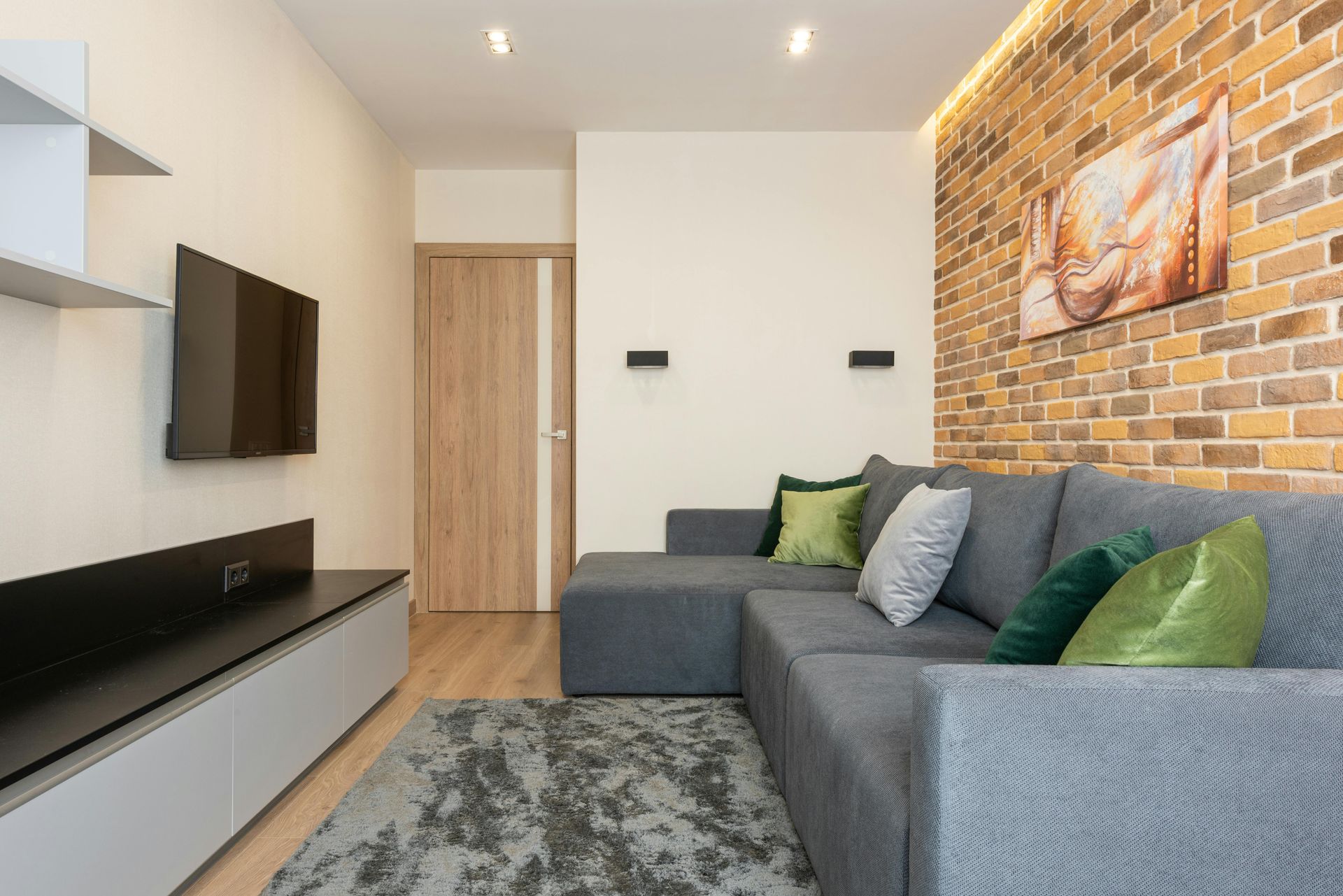 A living room with a couch , rug , television and brick wall.