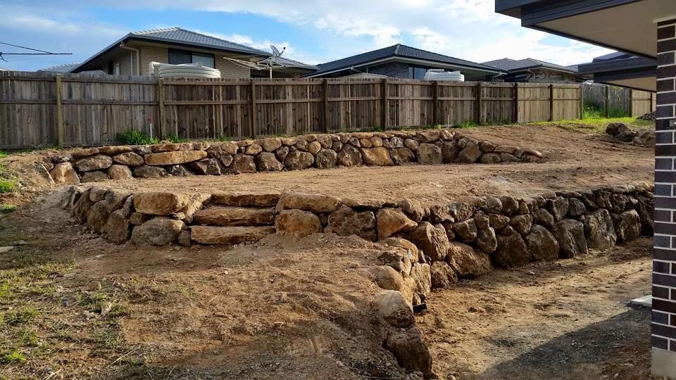 Rock Retaining Wall Behind a Pool With Tan Pavers and Sparse Plants — Border Rockwalls in Stotts Creek, NSW
