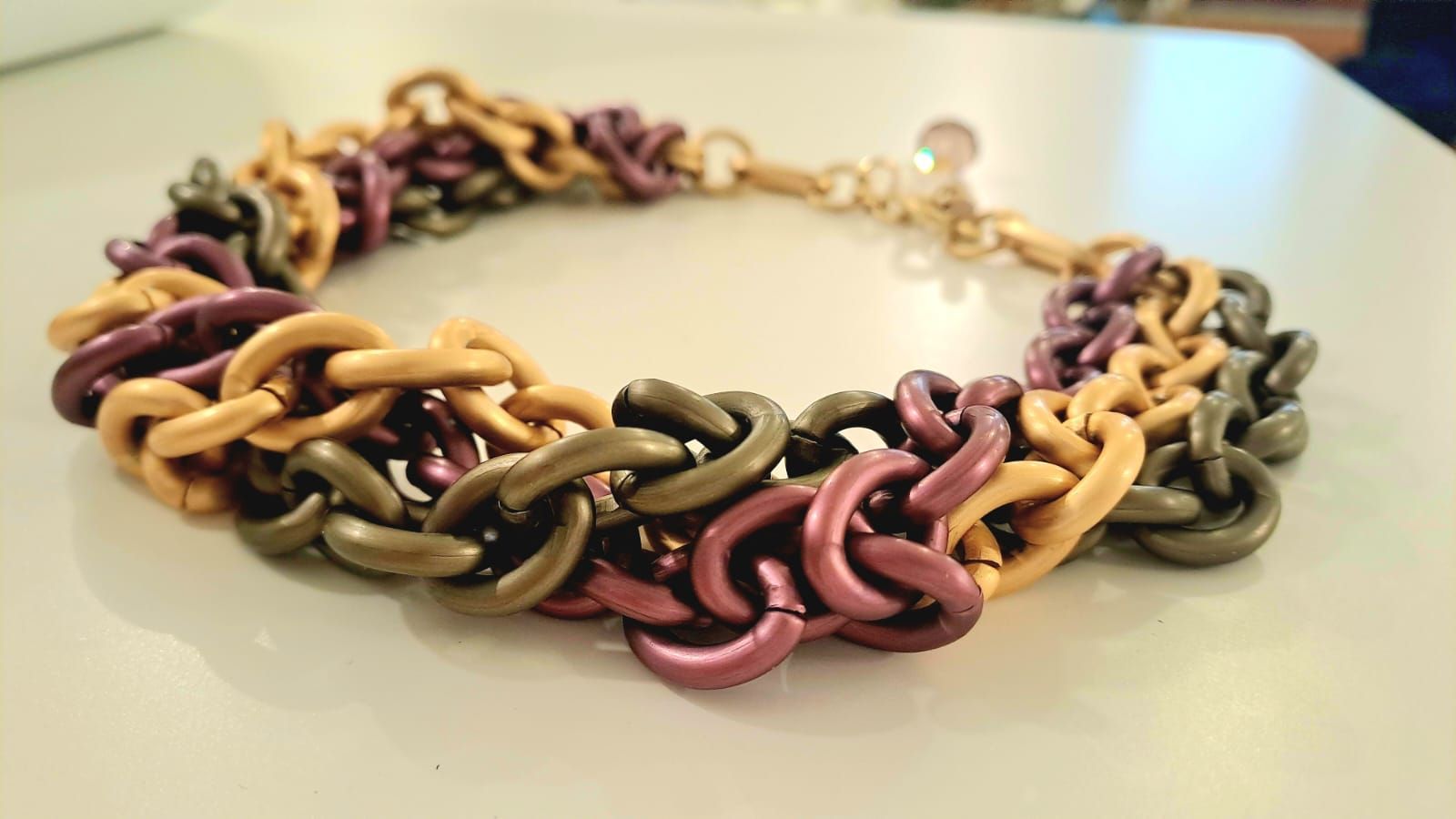 Bracciale con maglie intrecciate nei toni dell'oro, del viola e del verde.