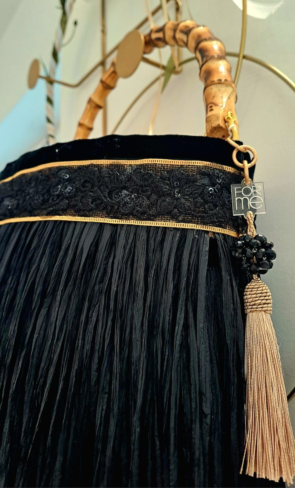Borsa nera con frange, manico in bambù, finiture dorate e nappa.