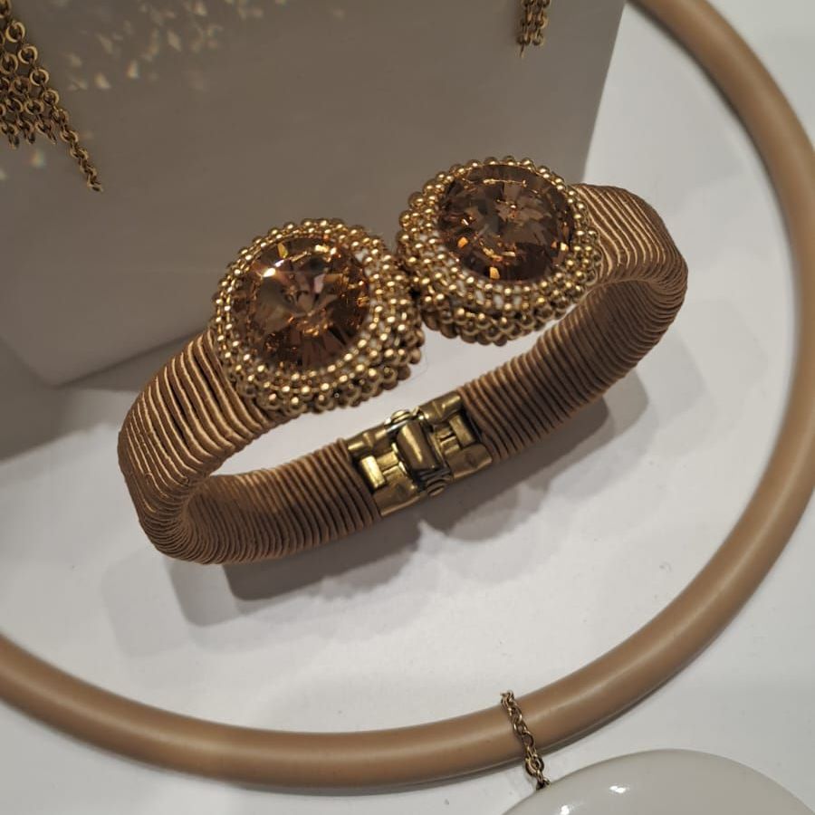 Bracciale color oro con due grandi gemme marroni, circondate da piccole perle, su una fascia a spirale con chiusura.