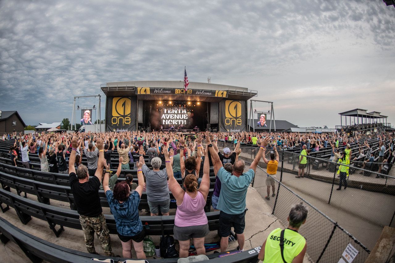 A crowd of people are standing in front of a stage with their hands in the air at the One Tenth Avenue North show. 