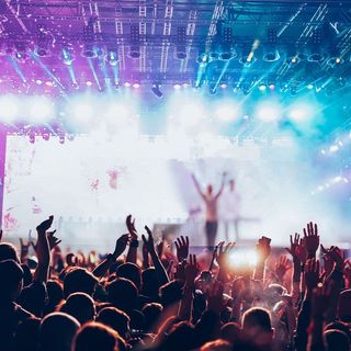 Concert crowd with arms raised toward a stage with bright lights.