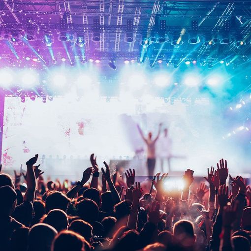 Concert crowd with arms raised toward a stage with bright lights.
