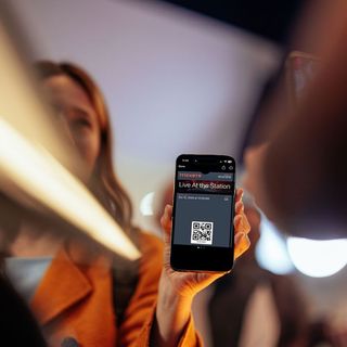 Woman holding smartphone with QR code at a train station.