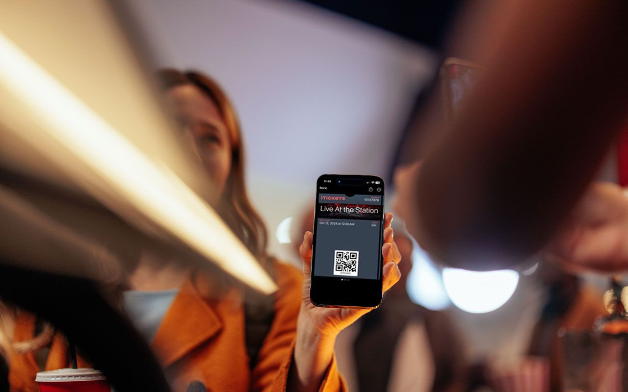 Woman holds phone with ticket app in a dim setting; blurred foreground and background.