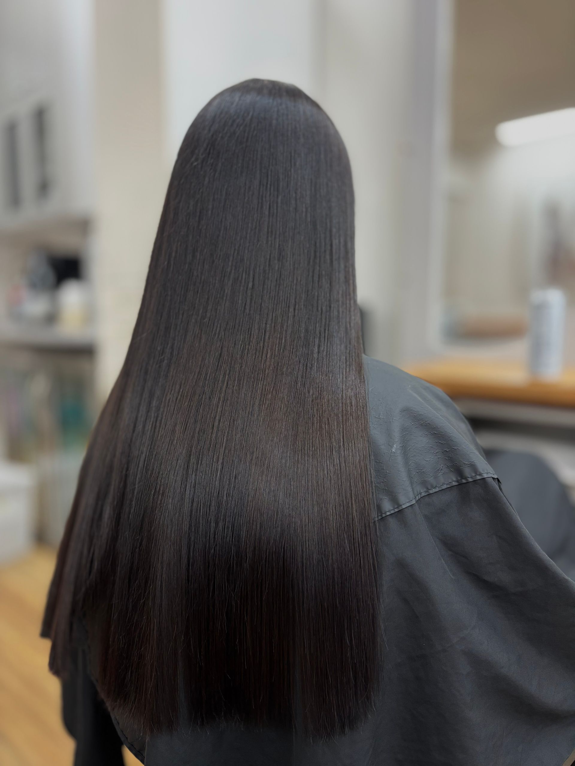 Close-up of a bob haircut with burgundy and red highlights, viewed from behind in a salon setting