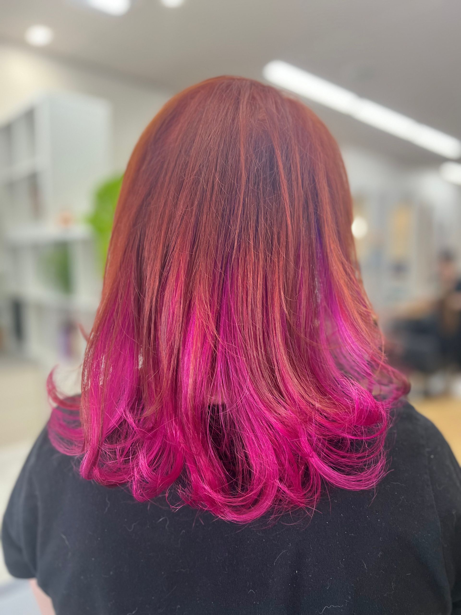 Back view of shoulder-length hair dyed burgundy and bright pink in a salon setting