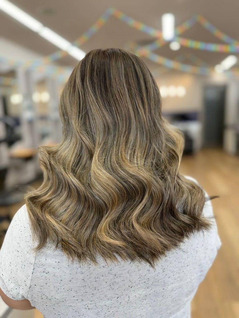Wavy, shoulder-length blonde-brown hair viewed from behind in a salon interior