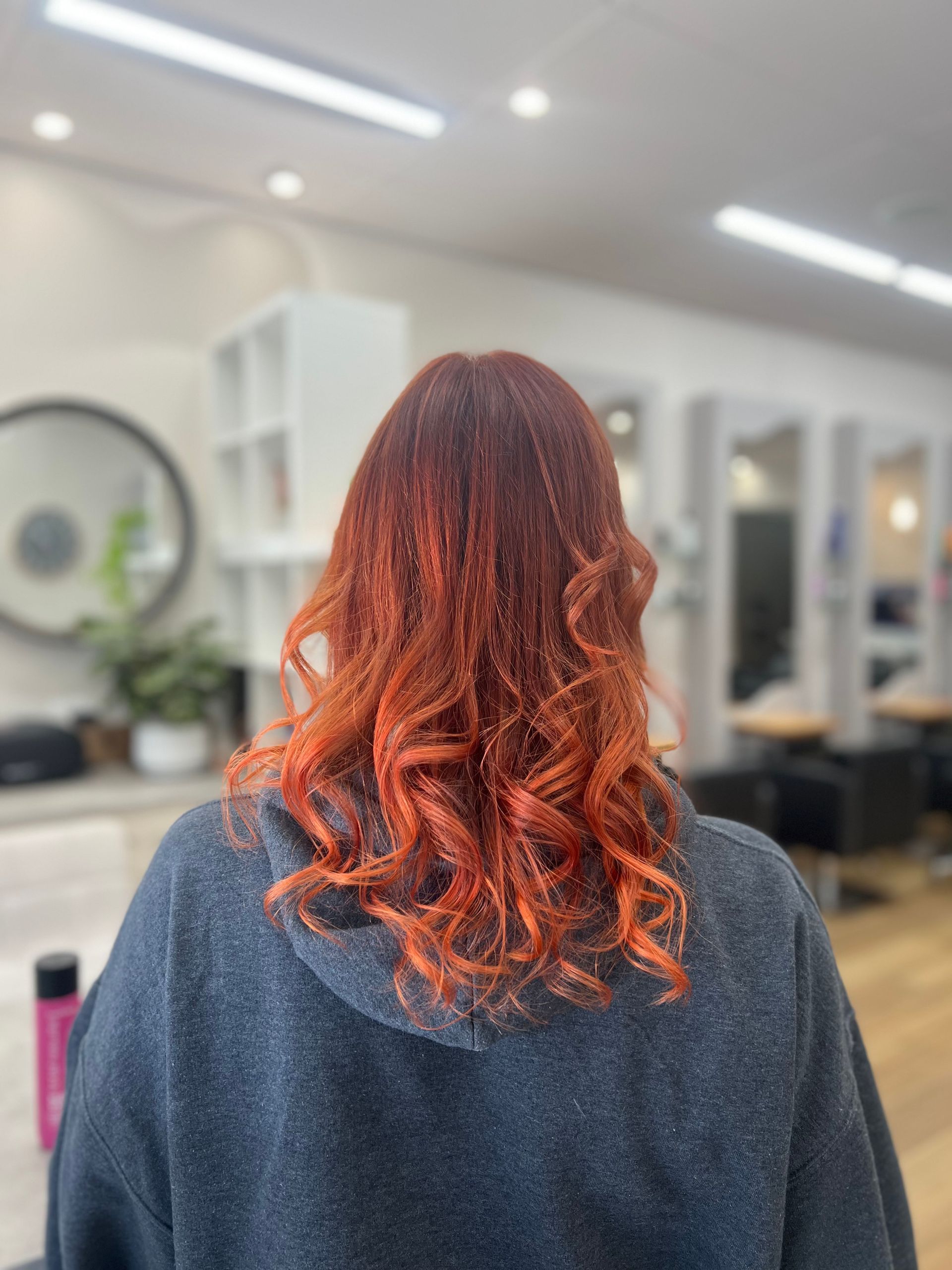 Back view of a person with curly red hair in a bright hair salon
